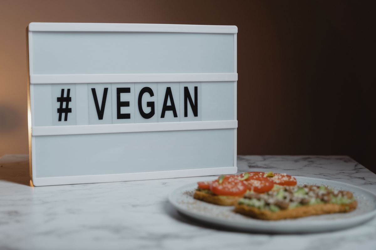 Illustrative stock photograph showing a lightbox sign reading hashtag vegan next to a slice of pizza